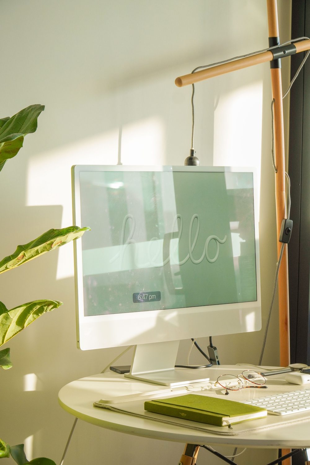 A sunlit desk with a monitor displaying 'hello', a plant, and a notebook